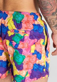 Shorts de bain colorés présentant un motif de oursons en gélatine répété dans des teintes pastel de vert, rose, jaune et violet, avec une taille élastique.