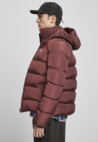 Bordo puffer jakna s kapuljačom, zatvaranjem na zip i prednjim džepovima. Materijal je gladak, s kviltanim dizajnom i logotipom na prsima.