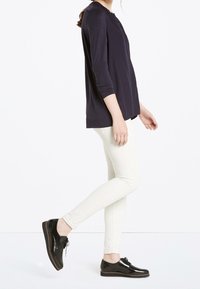 Maglia a maniche lunghe blu navy, pantaloni skinny color crema e scarpe oxford nere lucide. Gli abiti presentano un design semplice e una vestibilità rilassata.