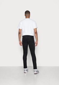 Jeans negros ajustados con un corte de talle medio, combinados con una camiseta blanca lisa. Modelo visto desde atrás, que presenta una textura suave y un detalle mínimo.