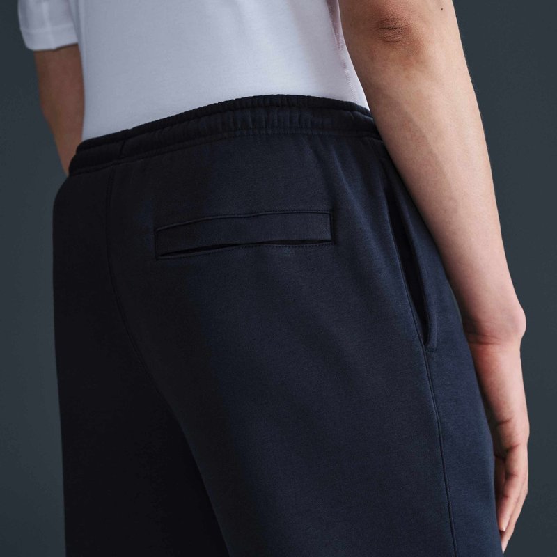 Persona che indossa una camicia bianca e pantaloni scuri con elastico in vita, vista da dietro con un braccio visibile e attenzione sulla tasca posteriore.