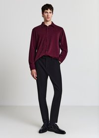 Dunkelrotes Langarmshirt mit dezentem Schimmer, geknöpft, kombiniert mit schwarzen, maßgeschneiderten Hosen und glänzenden schwarzen Lederschuhen.