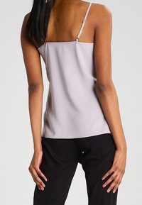 Lavendel camisole med tunna justerbara band, mjuk textur och avslappnad passform, kombinerad med svarta byxor.