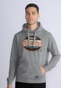 Sudadera gris con un bolsillo delantero, capucha con cordón y un diseño gráfico circular con texto en naranja y negro.