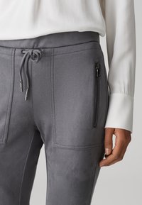 Graue Jogginghosen aus weichem, strukturiertem Stoff mit einem Kordelzugbund und einer mit Reißverschluss versehenen Tasche auf der linken Seite.