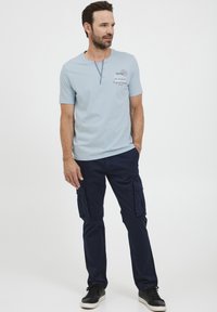 Lys blå kortermet skjorte med knappet henley-hals, kombinert med marineblå cargo-bukser med sidelommer og svarte joggesko.