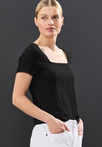 Must tekstuuriga lühikeste varrukatega ülaosa, millel on ruudukujuline kaelus. Kangas on õrnalt kootud, kombineeritud valgete pükstega.