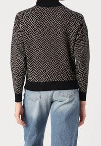 Pull en maille noir avec un motif géométrique beige. Comprend un col et des poignets côtelés foncés. Associé à un jean en denim bleu clair.