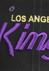Schwarze Kappe mit gesticktem Text: "LOS ANGELES" in Gold und "Kings" in Lila. Glattes Material mit sichtbaren Nahtdetails.