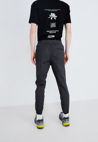 Černé tričko s grafickými motivy na zádech, doplněné tmavě šedými zúženými kalhotami s elastickým pasem a manžetami u kotníků.