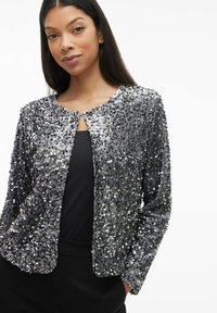 Sukienka z cekinami w odcieniach srebra i szarości, z okrągłym dekoltem, otwartym przodem i długimi rękawami z teksturowaną, błyszczącą powierzchnią.