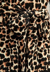 Luipaardprint stof met zwarte en oranje vlekken op een crèmekleurige achtergrond, vastgebonden met een bijpassende riem. Getextureerd, ribbelmateriaal.