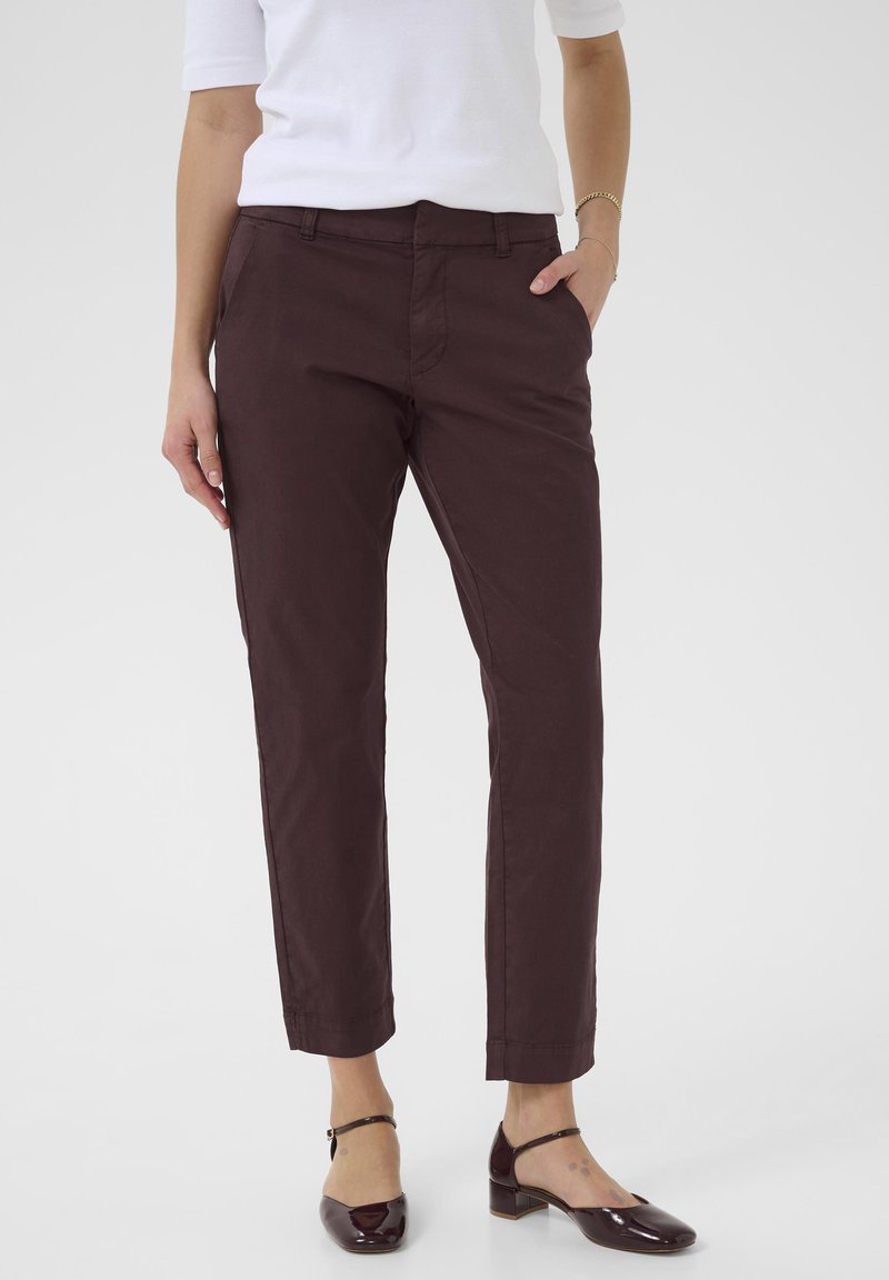 Pantalones burdeos oscuros de corte ajustado con un fit recto, detalles de bolsillos y dobladillos enrollados; combinados con unos zapatos de charol brillantes de tacón cuadrado.