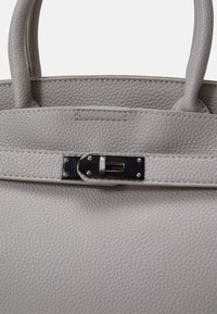 Grau strukturiertes Lederhandtasche mit zwei Griffen, ausgestattet mit einem Metallverschluss und Nähdetails, die ein strukturiertes Design schaffen.