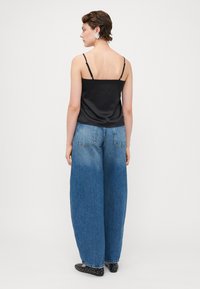 Svart sateng-camisole med tynne stropper, kombinert med løse lyseblå denim bukser med bredt ben. Sorte sko med nagler fullfører stilen.