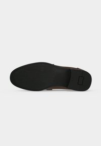 Semelle d'une chaussure habillée en cuir marron montrant un dessous en caoutchouc noir avec talon texturé et avant-pied lisse sur fond clair.