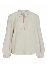 Blusa a maniche lunghe in crema con colletto alto, spalle arricciate e un dettaglio legato sul davanti. Realizzata in un tessuto leggero e texturizzato.