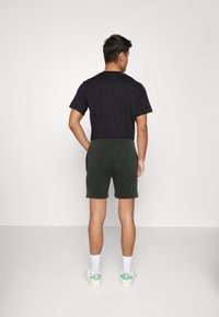 Zwarte t-shirt en donkergrijze shorts. De shorts hebben een elastische tailleband, zijzakken en een gladde textuur. Witte sokken en sneakers met groene accenten.