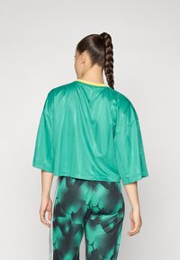 Green cropped shirt with a shiny texture and short sleeves, featuring a yellow collar, paired with patterned high-waisted leggings.