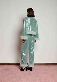 Sequined two-piece set in mint green, featuring a cropped jacket with faux fur cuffs and matching pants, complemented by black heels.