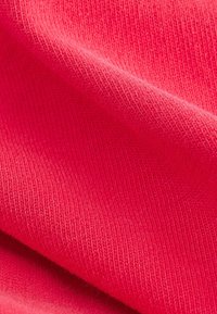 Helles pinkes Gewebe mit einer glatten, weichen Textur, das ein geripptes Muster und einen leichten Glanz aufweist, gefaltet, um Tiefe und Dimension zu zeigen.