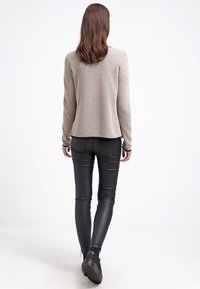 Béžový pletený svetr s texturou a dlouhými rukávy, doplněný o černé kalhoty ze syntetické kůže. Tento outfit obsahuje jemné švy.