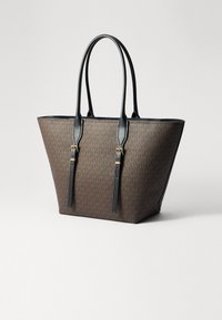 Brun tote taske med et monogrammønster, sorte læderdetaljer, to håndtag og et strømlinet, tapet design. Detaljer i guldtonet metal.