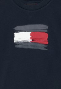 Camiseta navy con diseño de pinceladas en rojo, blanco y gris. Material de algodón suave con cuello redondo y mangas cortas.