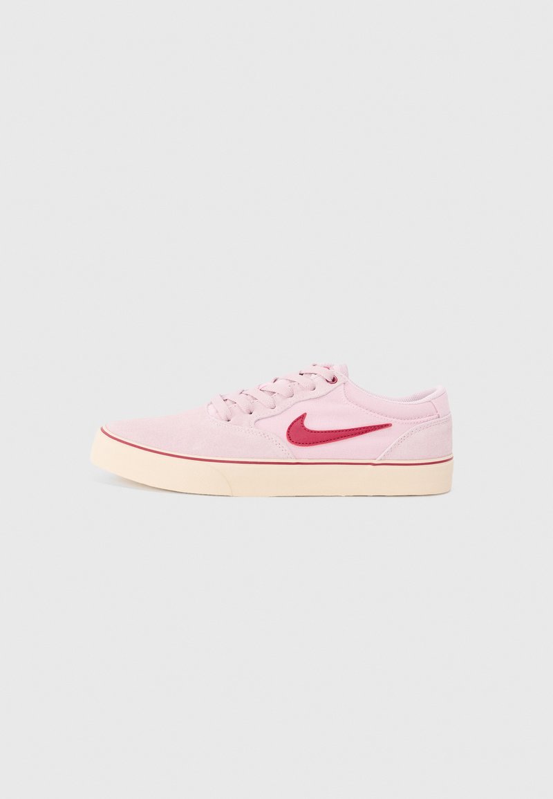 Sapatilha de camurça cor de rosa claro com o logo da Nike em vermelho, bico redondo, sola de borracha creme plana e costura contrastante em vermelho ao longo da borda.