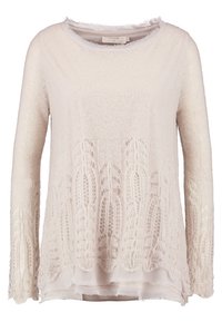 Ljusbeige stickad tröja med långa ärmar, med ett spetsmönster i nederkant och ett lager-på-lager-utseende med en genomskinlig underdel.