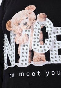 Czarna koszulka z beżową grafiką misia o miękkiej strukturze oraz zdobieniami z kryształków układającymi się w biały napis "NICE".