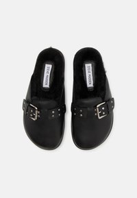 Sabots en cuir noir avec un doublure noire en peluche, dotés d'une boucle décorative et de clous en argent sur le côté pour plus de détails.