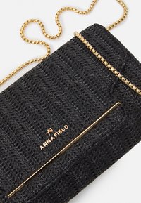 Černá pletená psaníčko s texturovaným vzorem, s zlatým řetízkem a akcentem, a s embosovaným názvem značky "ANNA FIELD" ve zlaté barvě.