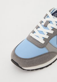 Light blue and gray athletic shoe with suede and textile materials, featuring white laces, a grey accent panel, and a black rubber sole.