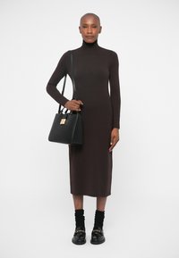 Robe midi en maille côtelée couleur marron à col roul�é. Sac à main noir avec quincaillerie dorée. Chaussettes et chaussures noires complètent le look.