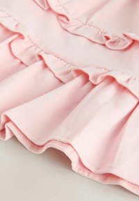 Blødt lyserødt stof med flere lag af flæser og pæn syning langs kanterne, der viser materialets struktur og detaljer.