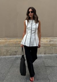 Valge ilma varrukateta topp mustade vertikaalsete triipudega, peplumi siluett, sobitatud mustade laia jala pükstega ja punaste plätudega. Kandmas tekstuuriga musta kotti.