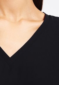 Black v-neck garment, smooth texture, lightweight fabric, visible stitching along the edges, close fit around the neckline.