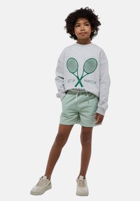 Sweat-shirt gris avec un motif de raquette de tennis verte, associé à un short rayé vert et blanc et des baskets beiges. Tenue décontractée pour enfants.
