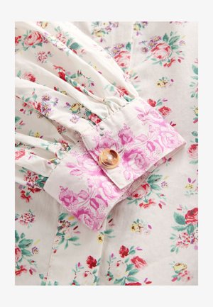 Valge kangas mitmevärvilise lillemustriga, kardoniga kogutud mansett roosa lillemustriga ja pruunikaskollase marmoorse nööpidega sulgemiseks.