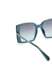 Occhiali da sole quadrati con una montatura traslucida color teal, lenti sfumate e dettagli dorati sulle tempie. Texture liscia con uno stile elegante.