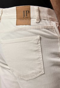 Jeans de denim blanco con un acabado texturizado, que cuentan con una etiqueta de cuero marrón con "JP 1880" en la parte trasera de la cinturilla y un bolsillo trasero.