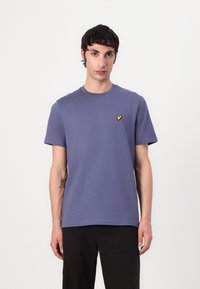Lila bomull t-shirt med kort ärm och rund halsringning, med en liten gul fjärilslogga på vänster bröst.