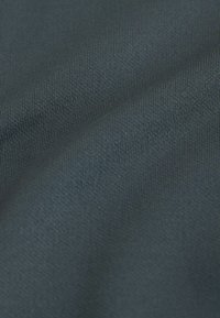 Gros plan sur un tissu gris foncé à texture côtelée fine avec de légers plis formant des lignes courbes à la surface.