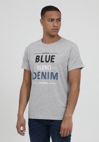 Camiseta de manga corta gris con la inscripción "VINTAGE BLUE BLEND DENIM ORIGINAL" impresa en texto en contraste negro y azul. Presenta un cuello redondo.