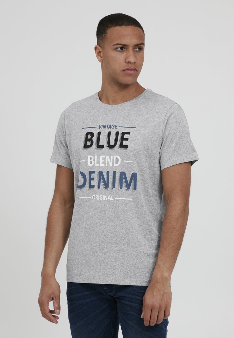 Camiseta de manga corta gris con la inscripción "VINTAGE BLUE BLEND DENIM ORIGINAL" impresa en texto en contraste negro y azul. Presenta un cuello redondo.