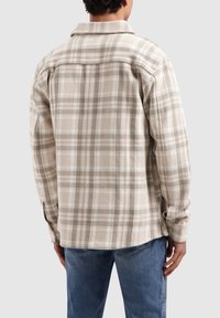 Beige geruit shirt, lichtgewicht stof, knoopsluiting, met grote ruitpatronen in bruin en roomwitte kleuren, voorzien van een omgeslagen kraag en manchet details.