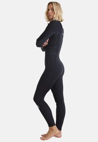 Svart våtdräkt med långa ärmar, med en strukturerad svart design på axlar och sidor, tillverkad av strechigt material för vattenaktiviteter.