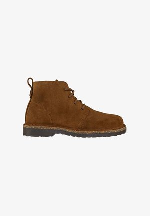 Bottine en suède marron avec un bout rond, un design à lacets et une semelle en caoutchouc texturé avec un accent en liège. Tirant à l'arrière.
