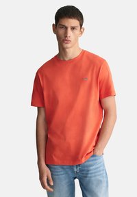 Kortermet oransje bomulls T-skjorte med rund hals og en liten brodert logo på brystet, kombinert med lyseblå denimjeans.